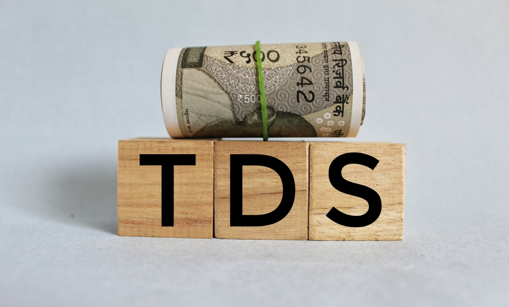 Indian currency roll placed on wooden blocks with the letters TDS (Tax Deducted at Source)