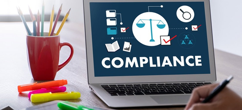 Laptop displaying compliance icon with legal symbols beside office supplies.